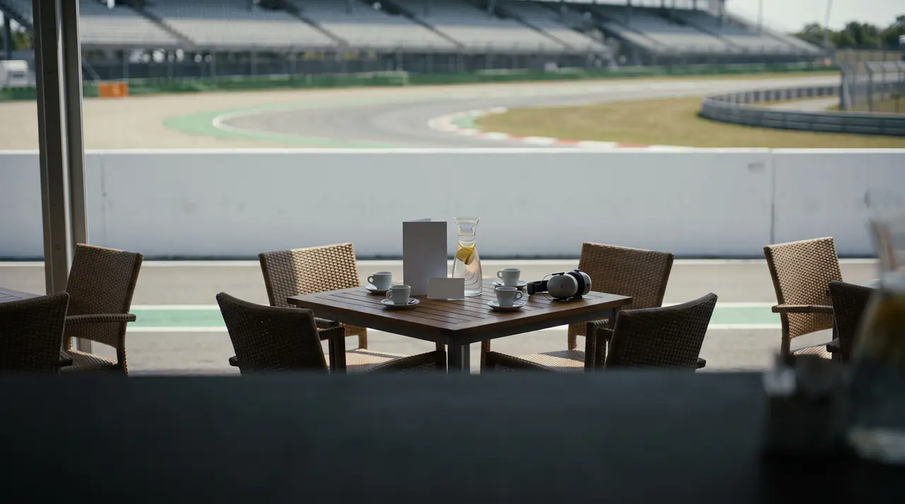 Coffee and ear defenders on a shaded terrace table beside a sweeping circuit corner