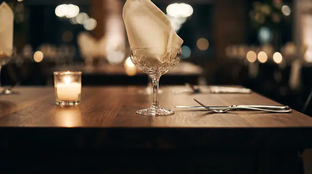 A crystal coupe holding a folded napkin beside a candle on a walnut table